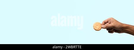 Male hand holding a biscuit on light cyan background banner. Stock Photo