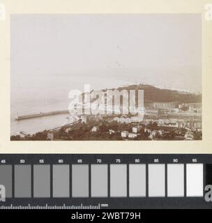 View of a harbor entrance with lighthouse, presumably on the coast of southern France, c. 1900 - c. 1910 photograph Part of photo album of a French amateur photographer with recordings of a family, Distillery Delizy & Doistau Fils, the army and sights in France. South France paper. photographic support  lighthouse, lightship. coast. prospect of city, town panorama, silhouette of city South France Stock Photo