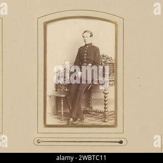Portrait of a young man in uniform with cap in hand, leaning on a writing table, Leopold Wallnau, 1850 - 1900 Photograph. visit card This photo is part of an album. Berlin cardboard. photographic support albumen print historical persons. (military) uniforms. uniform cap. writing-table, writing-desk Stock Photo