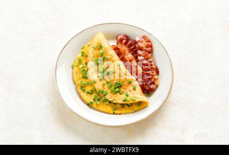 Omelet with cheese, green onion and roasted bacon on plate over light background. Tasty healthy dish for breakfast. Close up view Stock Photo