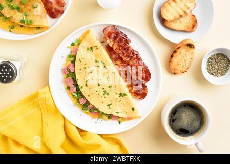 Stuffed omelette with ham and green onion on white plate over light background. Served with roasted bacon. Tasty meal for breakfast. Top view, flat la Stock Photo