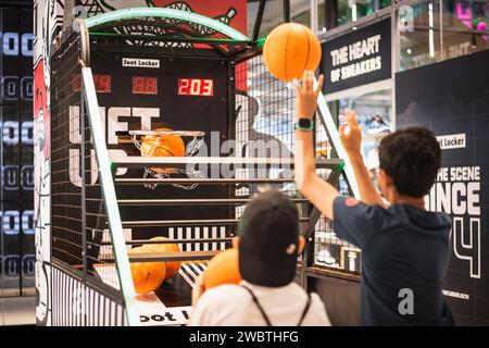 Bangkok, Thailand - December 17, 2023: two boys play basketball arcade game machine at Foot Locker store at EmSphere shopping mall. Stock Photo