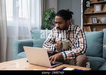 Focused young African American freelance businessman study online watching webinar podcast on laptop listening learning education course conference ca Stock Photo