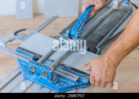 Construction worker cuts ceramic tile using tile cutting hand machine. Stock Photo