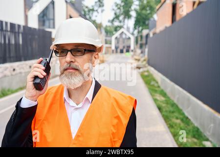 Serious foreman using hand-held radio transceiver on development site Stock Photo