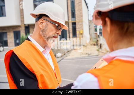 Construction staff in hard hats scrutinizing documents on development site Stock Photo