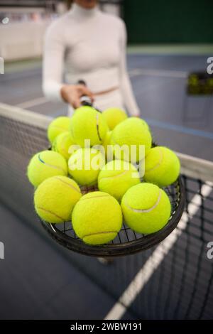 Unknown woman player in white attire holding lots tennis balls on racket Stock Photo