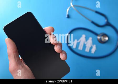 Family healthcare phone care concept with hand holding a smartphone and stethoscope and cutout of family in the background on blue background. Top vie Stock Photo