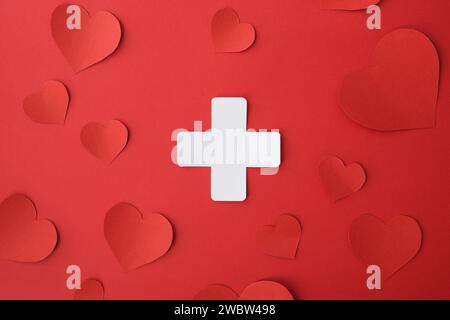 Conceptual medicine symbol with cross shaped paper cutout isolated in the center on red background. Stock Photo