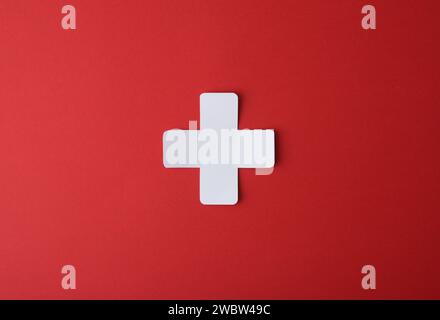 Conceptual medicine symbol with cross shaped paper cutout isolated in the center on red background. Stock Photo