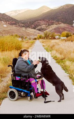 Woman uses her electric wheelchair to navigate the walking path in the small mountain town of Salida, Colorado, USA Stock Photo