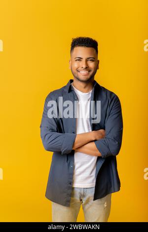 Nice smiling indian male entrepreneur isolated on yellow, portrait of happy determined male student looking at camera with arms crossed, arab man posing in studio Stock Photo