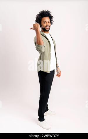 Smiling cheerful young man points aside and looking at the camera with cheerful wide toothy smile, guy presenting novelty, advertising, isolated on white wall Stock Photo