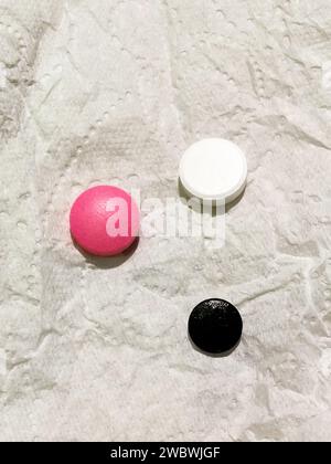 White, black and pink medical pill on a white paper napkin. Concept of medicine and pharmacy. Top view. Copy space. Stock Photo