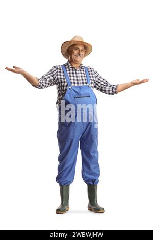 Full length portrait of a mature farmer in blue overalls gesturing welcome isolated on white background Stock Photo