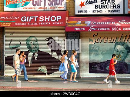 Tourists walk past images of Hollywood icons painted on storefront shutters on Hollywood Blvd., LosAngeles, CA, USA Stock Photo