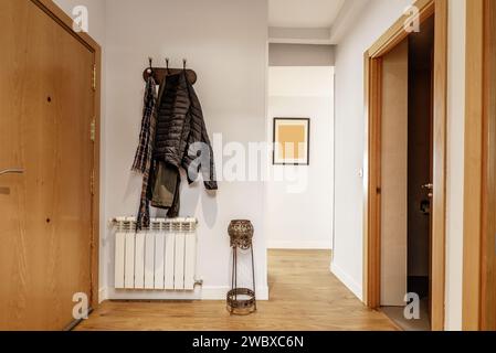 Hallway of a home with armored access door, an aluminum radiator, wooden floors and a coat rack with hanging clothes Stock Photo