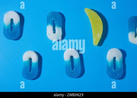 array of two lines of 0 shaped white and blue gummy candies on a blue background, one of them being substituted by a banana gummy, laying in a horizon Stock Photo