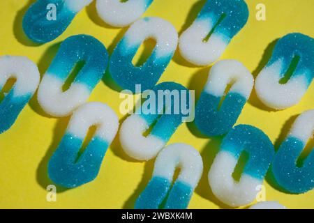 array of several lines of 0 shaped white and blue gummy candies on a yellow background, horizontal image with harsh light. tilted view. Stock Photo
