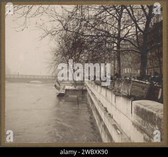 People look from behind book stalls on the quay the high water level of the Seine in Paris, G. Dangeux, 1910 photograph Part of photo album flooding Paris and suburbs 1910. Paris photographic support  flood (+ landscape with figures, staffage). pier, quay, wharf. book-stall, kiosk Paris Stock Photo
