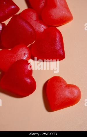 Red heart-shaped candies resting on a pastel orange surface, one of them is separated Stock Photo