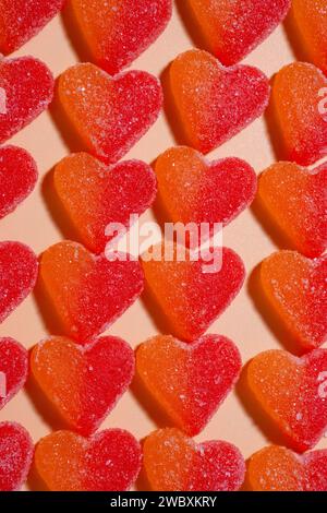 Array of heart-shaped orange and red gummies. laying on a pastel orange surface. Upside view, horizontal image Stock Photo
