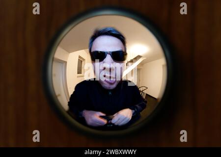 view through door viewer into a staircase, peephole, spyhole, with a man in front of the door, looking very angry, maybe landlord or bailiff Stock Photo