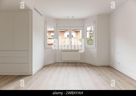 A newly renovated room with white wooden cabinets, a large gallery with white aluminum windows, radiators underneath and light wooden flooring Stock Photo