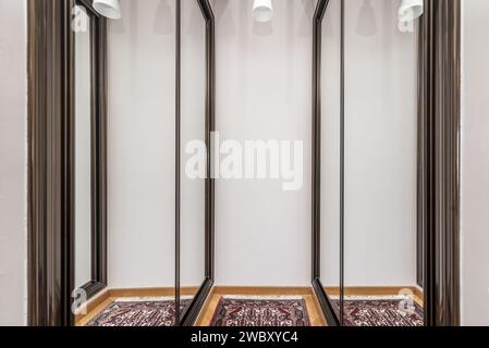 A room with a dressing space with built-in wardrobes with sliding mirror doors and a rug on the floor Stock Photo