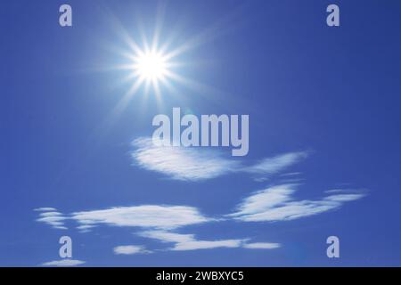 sun in blue sky with some white  lenticular clouds Stock Photo
