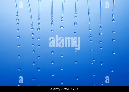 closeup, macro of several water jets, drops or droplets falling down, before blue background Stock Photo