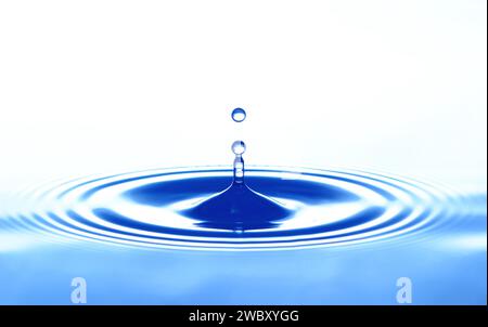 closeup, macro of water drop dripping on a water surface, causing circular waves Stock Photo
