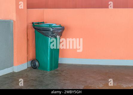 Concept of cleaning, waste separation, and public hygiene. Trash bin on cement floor with orange wall background, recycle concept. Stock Photo
