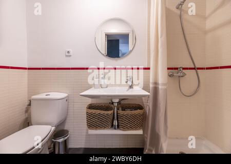 Frontal image of a small bathroom with white porcelain tiles, circular mirror built into the wall and shower cabin with curtain Stock Photo