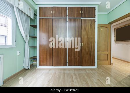 An empty room with light green painted walls, plaster moldings on the ceiling and a large built-in wardrobe with wooden doors and mezzanines Stock Photo