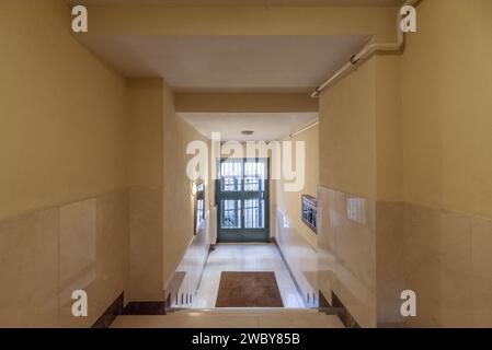 Portal of a building with a metal door, floors and walls tiled in cream-colored marble and a natural gas connection Stock Photo