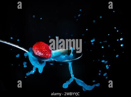 Strawberry splashing into a milky blue liquid in a spoon Stock Photo