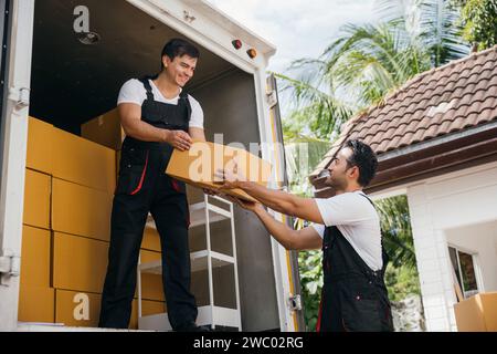 Young delivery men unload boxes from a van. Movers in uniform work together delivering orders Stock Photo