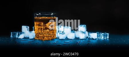 Glass of whiskey against melting ice cubes on dark background Stock Photo