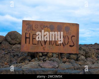 Metal sign to Los Hervideros. Cultural site and tourist attraction. Lava rocks near Timanfaya National park. Canary Islands, Lanzarote, Spain Stock Photo