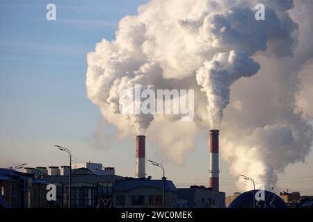 Factory chimneys with white smoke on blue sky background above the city buildings. Air pollution, heating season in winter Stock Photo