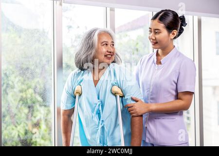 An attentive nurse engages in conversation with a senior woman using crutches for support Stock Photo