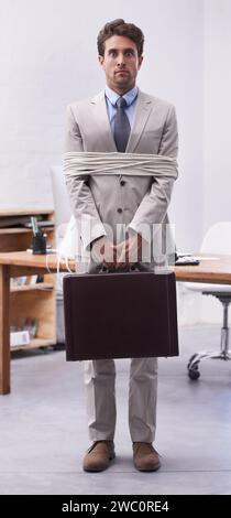 Scared businessman in office tied up in rope with depression, control and prisoner in law firm. Serious attorney, lawyer or legal consultant bound at Stock Photo