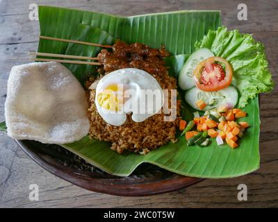 Fried Rice or Indonesian Nasi Goreng served on a banana leaf with chicken satay, fried egg and pickles. Stock Photo