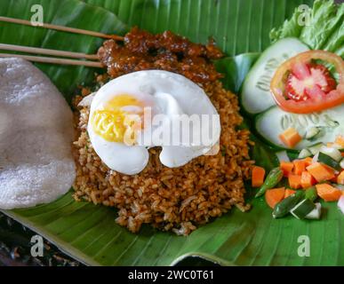 Fried Rice or Indonesian Nasi Goreng served on a banana leaf with chicken satay, fried egg and pickles. Stock Photo