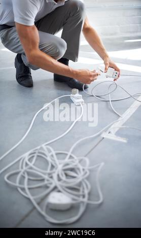 Hands, man and electrician plug connection, power and electricity in office. Cord, wire and cable on floor, socket and energy of worker, professional Stock Photo