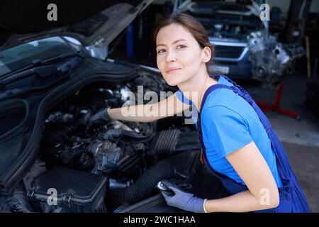 Female mechanic works in overalls under the hood of car Stock Photo