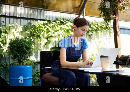 Female comfortably seated with coffee and laptop in garden chair Stock Photo