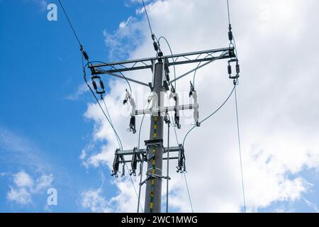 high voltage overhead line, pole with insulators and disconnectors, white clouds in the blue sky Stock Photo