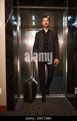 Happy guy with suitcase walking out elevator Stock Photo